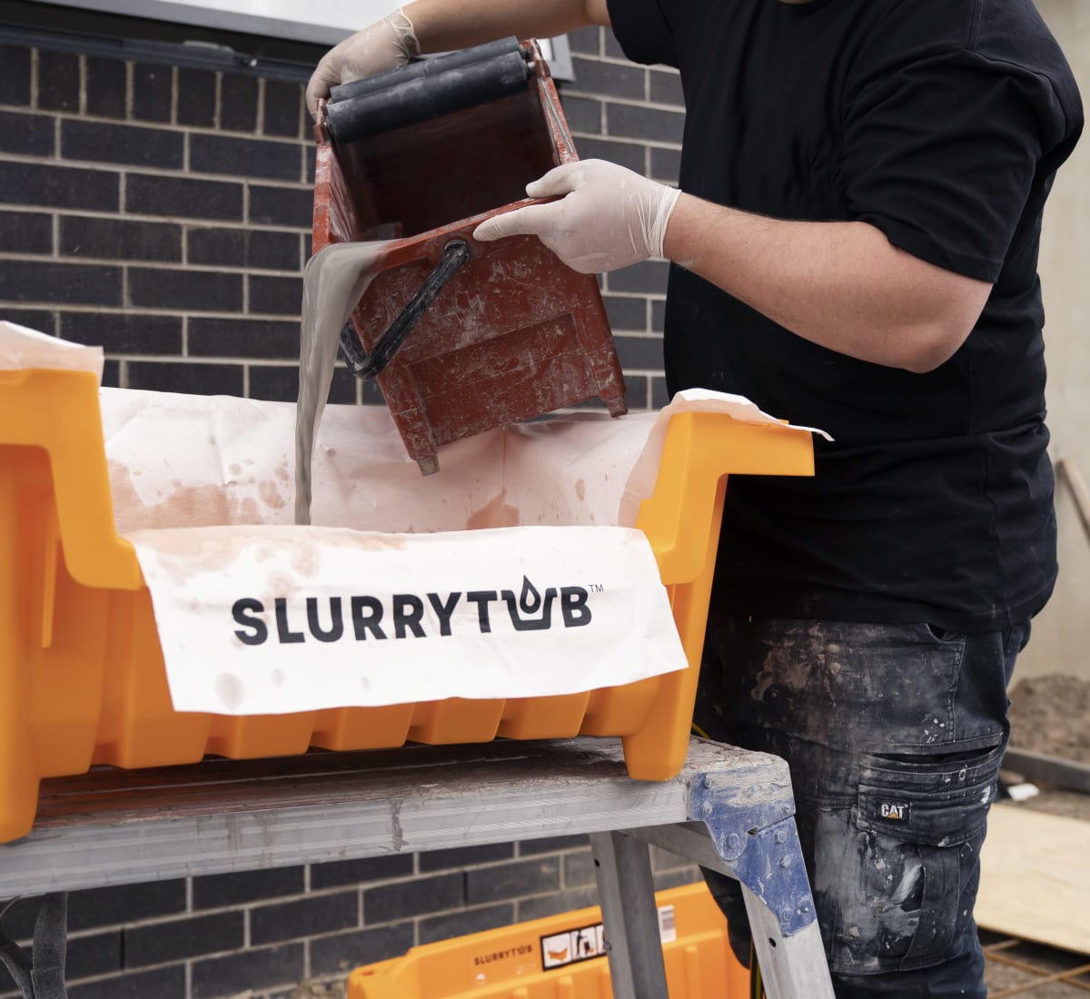 Person pouring slurry into an orange tub with a filter that says ‘SLURRYTUB’.